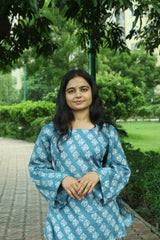 Back view of a woman in a teal blue block-printed short kurti, showing the square back neckline and tie-up detail with tassels.